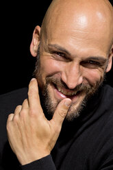Porträt eines lächelnden Mannes mit Finger auf dem Mund vor einem schwarzen Hintergrund - MAEF010888