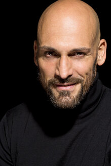 Portrait of bald man wearing black turtleneck in front of black background - MAEF010889