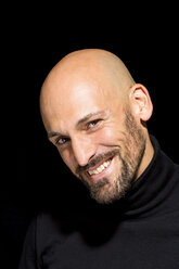 Porträt eines lächelnden Mannes mit Glatze und schwarzem Rollkragenpullover vor einem schwarzen Hintergrund - MAEF010890