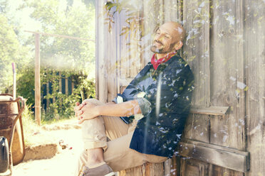 Man sitting in front of wooden hut daydreaming - MAEF010946