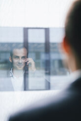 Spiegelung eines Geschäftsmannes, der auf einer Fensterscheibe telefoniert - BZF000186