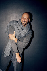 Portrait of smiling man with grey scarf in front of black background - MAEF010972