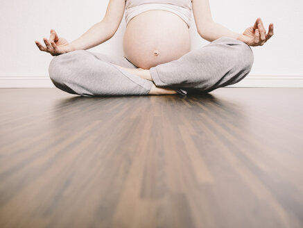 Schwangere Frau in Yoga-Position auf Holzboden - KRPF001625