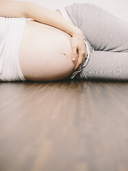 Pregnant woman resting on wooden floor holding her belly - KRPF001620