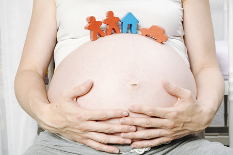 Pregnant woman in front of cot with toy house, toy figurines and toy car on her belly stock photo