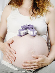 Schwangere Frau mit Babyschuhen auf dem Bauch - KRPF001606