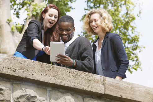 Drei glückliche Freunde im Freien teilen sich ein digitales Tablet - STKF001381