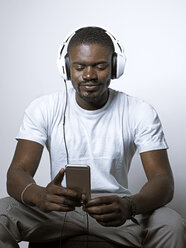 Lächelnder junger Mann mit Kopfhörern, der auf sein Mobiltelefon schaut - STKF001438