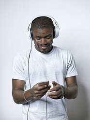 Smiling young man with headphones looking at cell phone - STKF001439