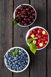 Three bowls of sour cherries, raspberries and blueberries on dark wood - CSF026133