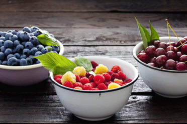 Three bowls sour cherries, raspberries and blueberries on dark wood - CSF026132