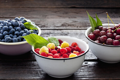 Drei Schalen Sauerkirschen, Himbeeren und Heidelbeeren auf dunklem Holz - CSF026132