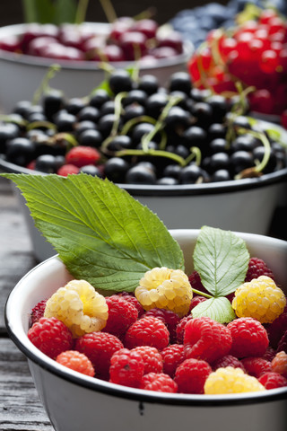 Schale mit roten und gelben Himbeeren und Schalen mit anderen Früchten im Hintergrund, lizenzfreies Stockfoto