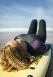 Spanien, Colunga, junge Frau auf Surfbrett liegend beim Sonnenbaden - MGOF000437