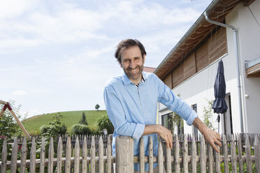 Portrait of smiling man standing in garden behind wooden fence - RBF003469