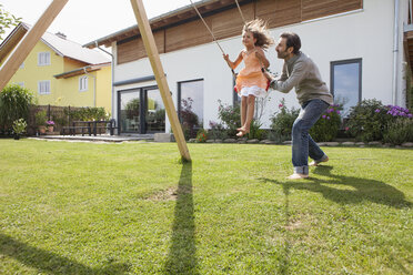 Vater schiebt Tochter auf einer Schaukel im Garten - RBF003479