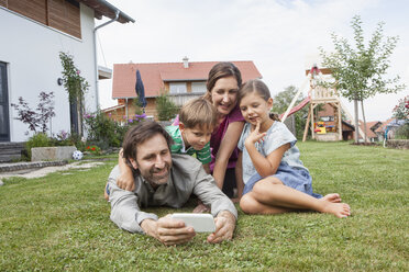 Lächelnde vierköpfige Familie im Garten mit Mobiltelefon - RBF003491