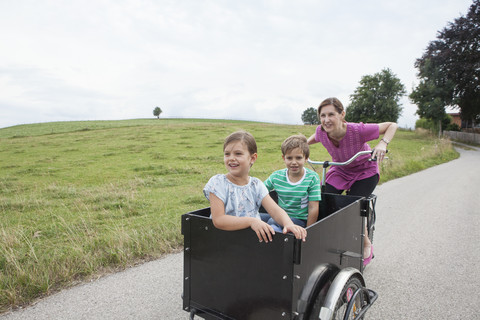 Mutter fährt Fahrrad mit Sohn und Tochter im Anhänger, lizenzfreies Stockfoto
