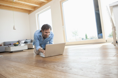 Älterer Mann zu Hause mit Laptop auf dem Boden, lizenzfreies Stockfoto