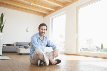 Mature man sitting at home on wooden floor, looking at camera - RBF003344