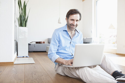 Mature man at home using laptop sitting on the floor - RBF003269