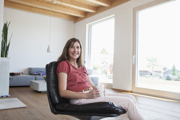 Reife Frau sitzt entspannt in ihrem Wohnzimmer und trinkt Kaffee - RBF003279