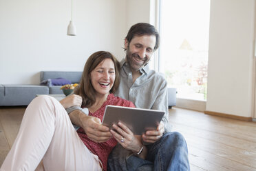 Mature couple sitting on floor, using digital tablet - RBF003290