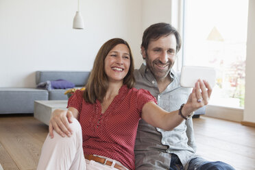 Mature couple sitting on floor taking selfie with smart phone - RBF003351