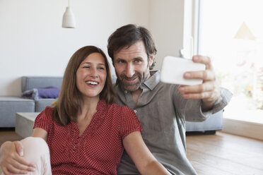 Mature couple sitting on floor taking selfie with smart phone - RBF003352