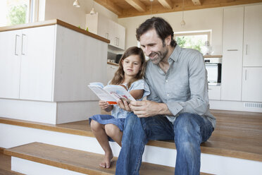 vater und Tochter sitzen auf den Küchenstufen und lesen ein Buch - RBF003308