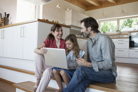 Happy family sitting on kitchen steps, daughter using laptop stock photo