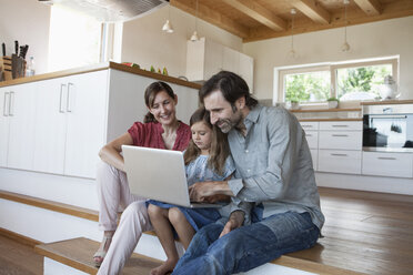 Glückliche Familie auf der Küchentreppe sitzend, Tochter am Laptop - RBF003311