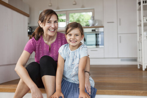Mutter und Tochter sitzen lächelnd in der Küche - RBF003335