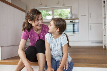 Mother and daughter sitting smiling in kitchen - RBF003336