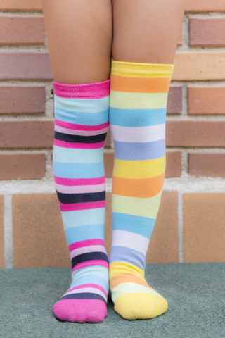 Füße eines Mädchens mit verschieden gestreiften farbigen Socken, lizenzfreies Stockfoto
