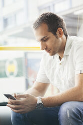 Mann sitzt in öffentlichen Verkehrsmitteln und schaut auf sein Smartphone - BZF000192
