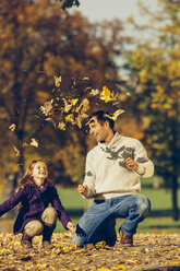 Porträt eines glücklichen Vaters und einer Tochter, die mit trockenen Blättern in einem Park spielen - CHAF001259