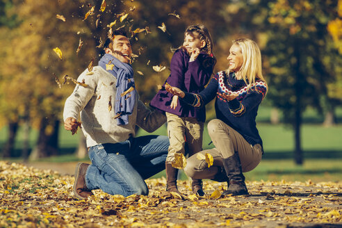 Eltern und Tochter spielen mit trockenen Blättern in einem Park - CHAF001072