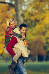 Mann nimmt seine Freundin im Herbst im Park huckepack - CHAF001160