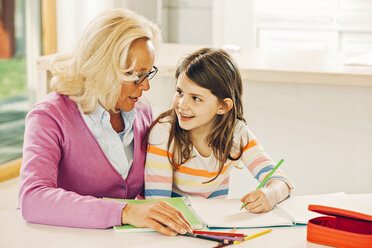 Grandmother and granddaughter sitting at table with coloring book - CHAF001110