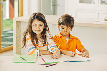 Schwester und Bruder sitzen am Tisch mit Malbuch - CHAF001559