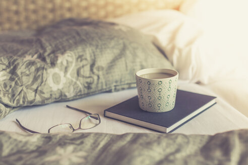 Book, reading glasses and cup of white coffee on bed - ASCF000321