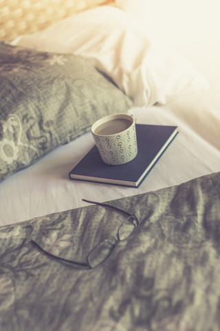 Buch, Lesebrille und Tasse Milchkaffee auf dem Bett, lizenzfreies Stockfoto