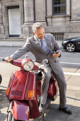 Germany, Stuttgart, smiling businessman sitting on motor scooter - JUNF000406