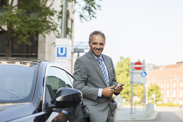 Deutschland, Stuttgart, Porträt eines lächelnden Geschäftsmannes, der sich an ein Auto lehnt - JUNF000408