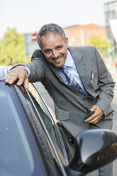 Porträt eines lächelnden Geschäftsmannes, der sich auf ein Auto stützt - JUNF000409