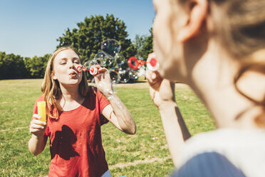 Two teenage girls blowing soap bubbbles in park - AIF000087