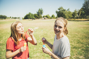 Two teenage girls blowing soap bubbbles in park - AIF000042