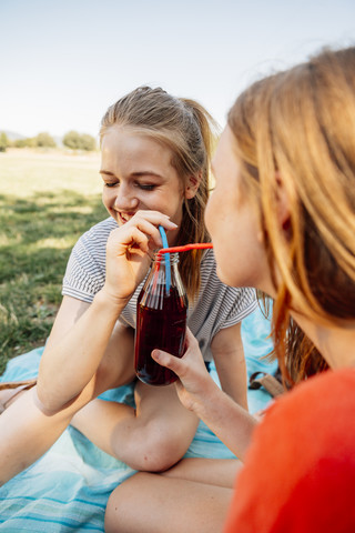 Two teenage girls sharing an ice tea in park stock photo