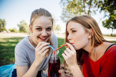 Two teenage girls sharing an ice tea in park stock photo